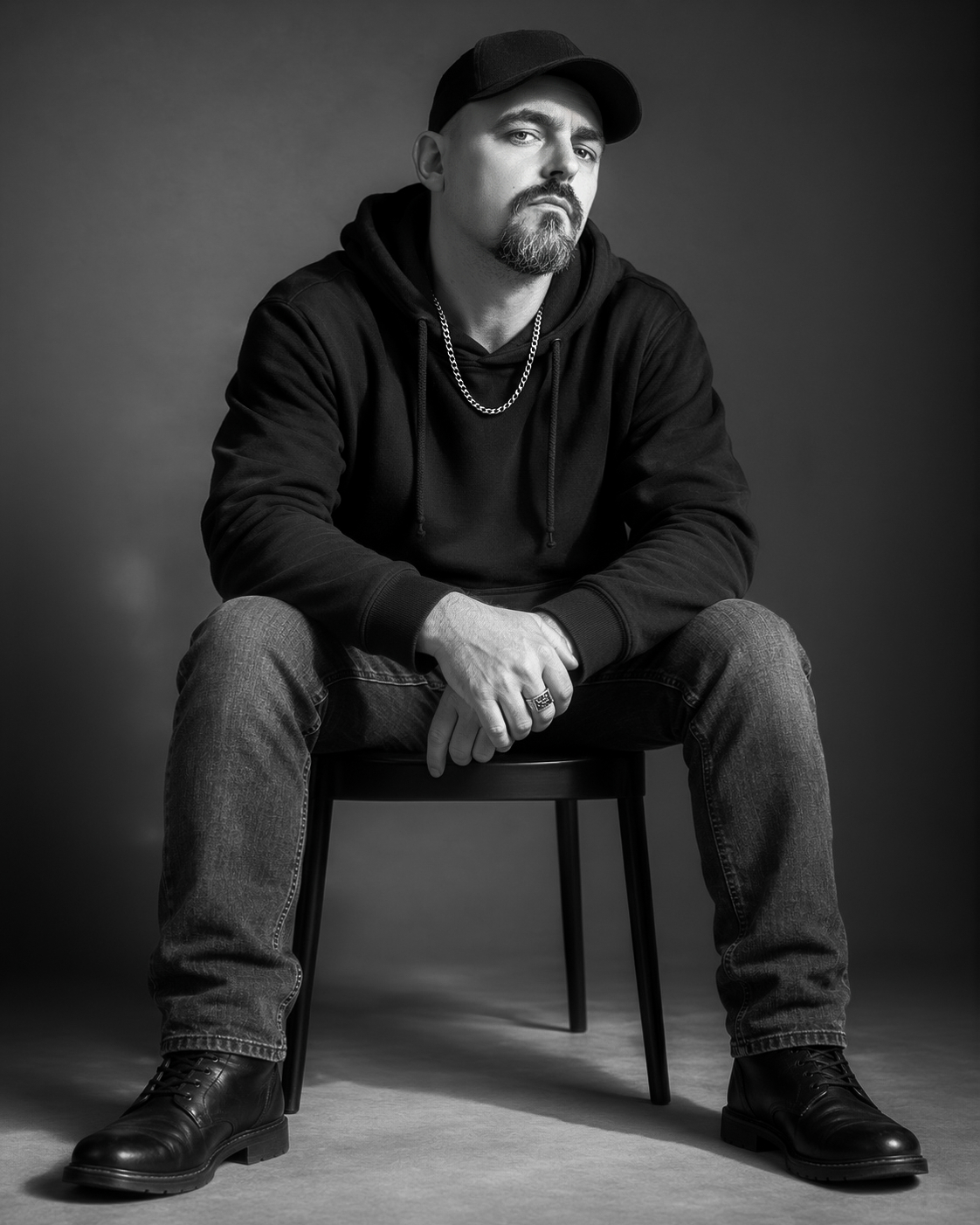 STE Stetson seated on a studio chair in a black hoodie and cap